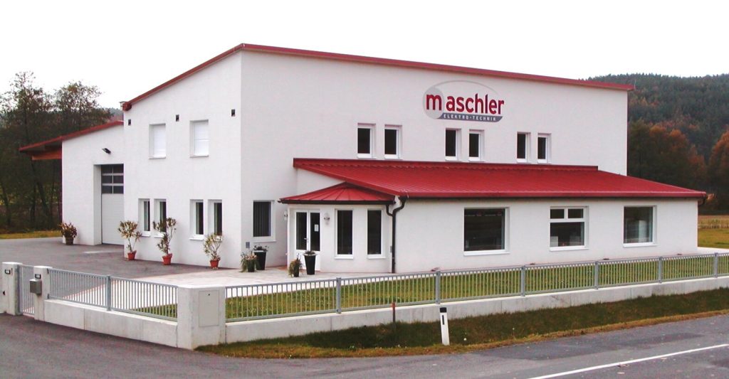 Modernes, weißes Büro- und Werkstattgebäude mit rotem Dach und Logo der Firma Maschler an der Fassade, umgeben von Natur.