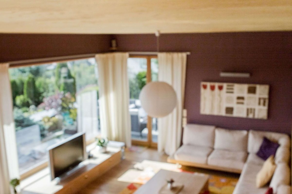 Rauchmelder an der Decke in einem Wohnzimmer mit gemütlicher Einrichtung, Fernseher und Sitzgelegenheit im Hintergrund.