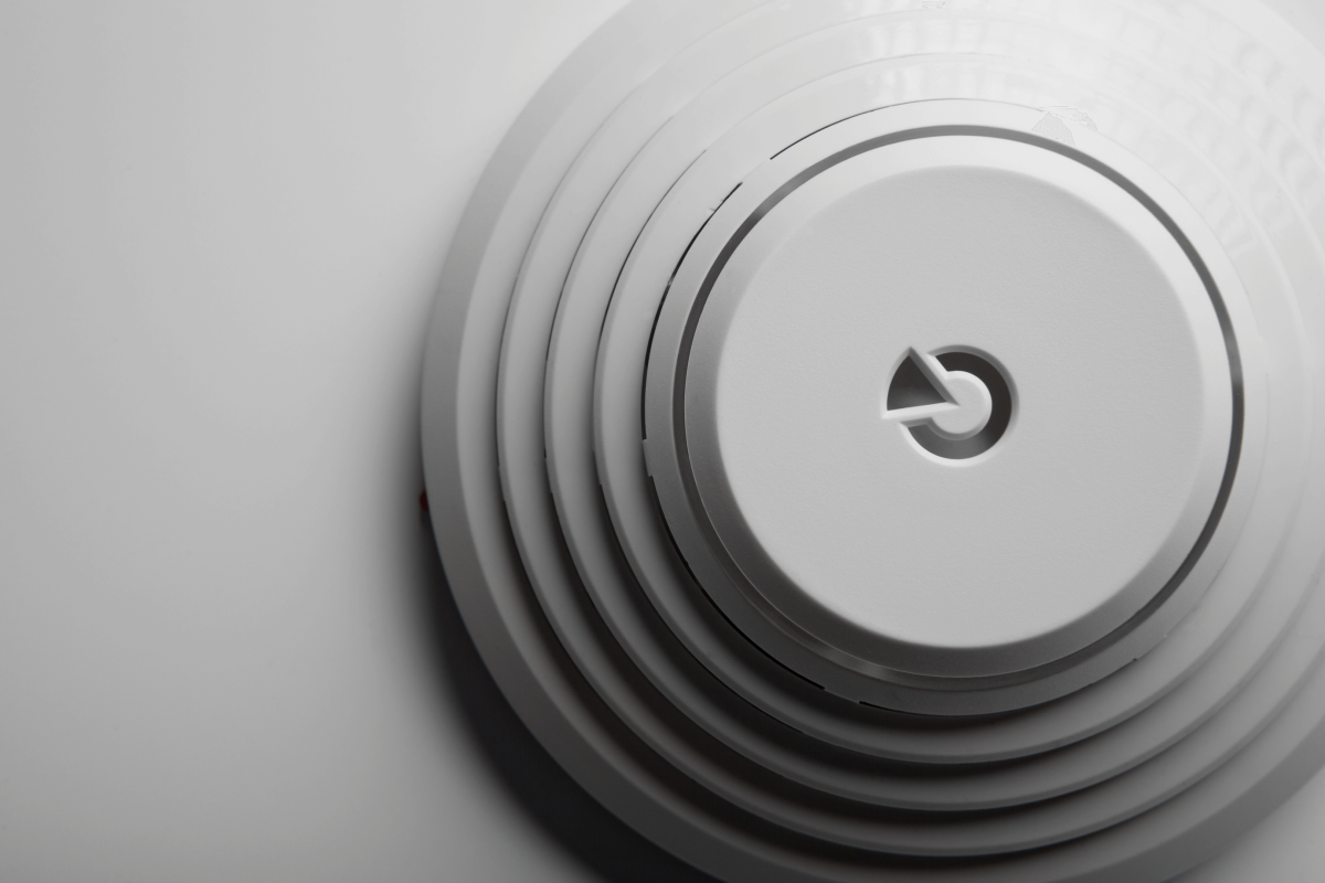 Moderne Nahaufnahme eines Rauchmelders mit konzentrischem Design und dezentem Logo in der Mitte.