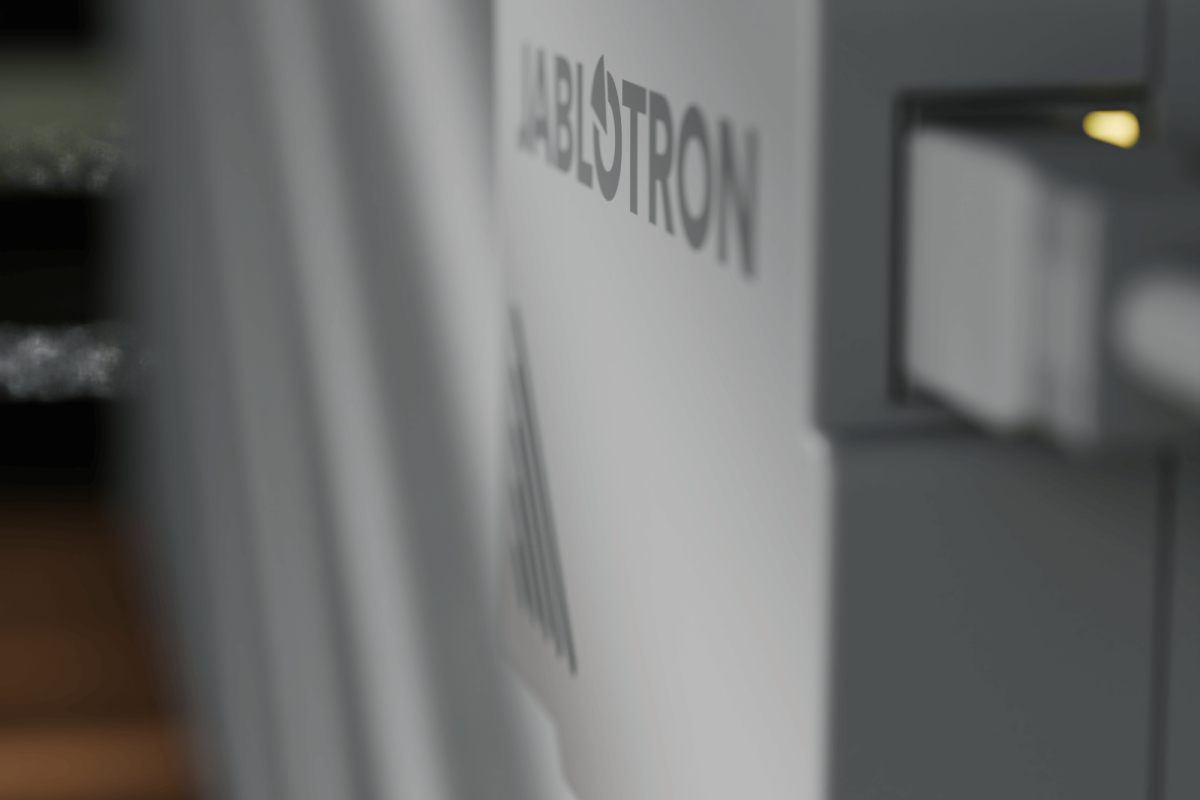 Nahaufnahme eines Jablotron Geräts an einer Wand mit einem gelben LED-Licht und sichtbarem Anschlusskabel.