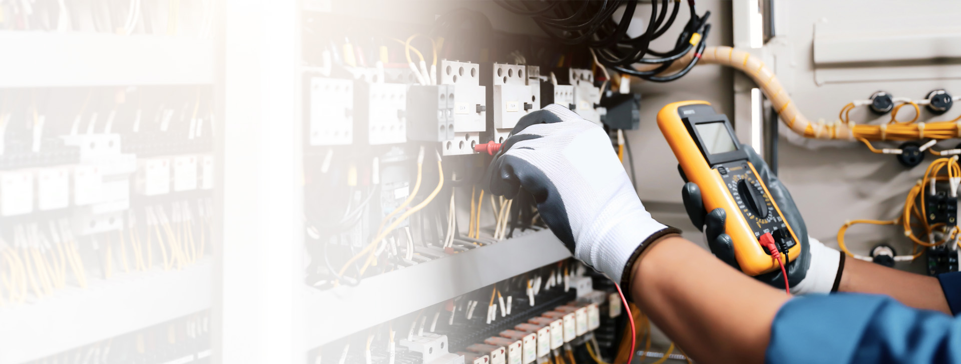 Elektriker bei der Prüfung einer Schalttafel mit einem Multimeter. Zu sehen sind Kabel, Schalter und die Hand mit Schutzhandschuhen bei der Arbeit.