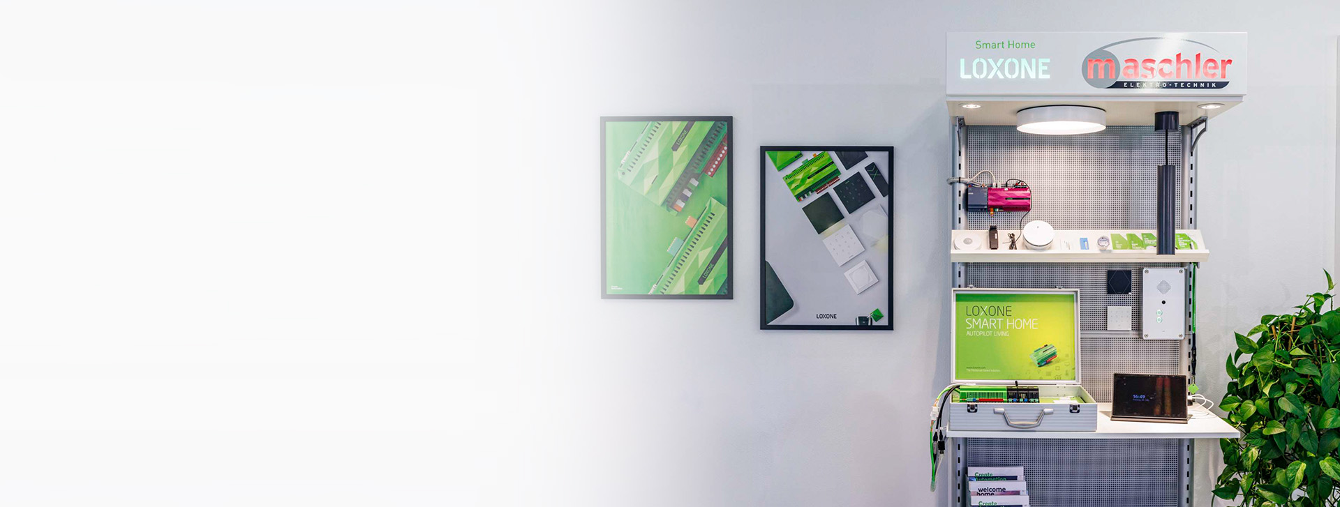 Präsentationswand mit Loxone Smart Home Technik bei Maschler. Zu sehen sind Steuergeräte, Sensoren, Tablets, Poster sowie das Maschler-Logo.